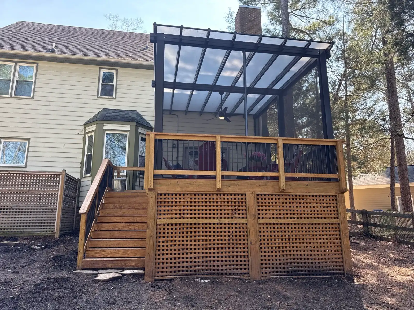 Elevated wood deck with stairs and a covered outdoor living area featuring a black frame and clear roof panels.