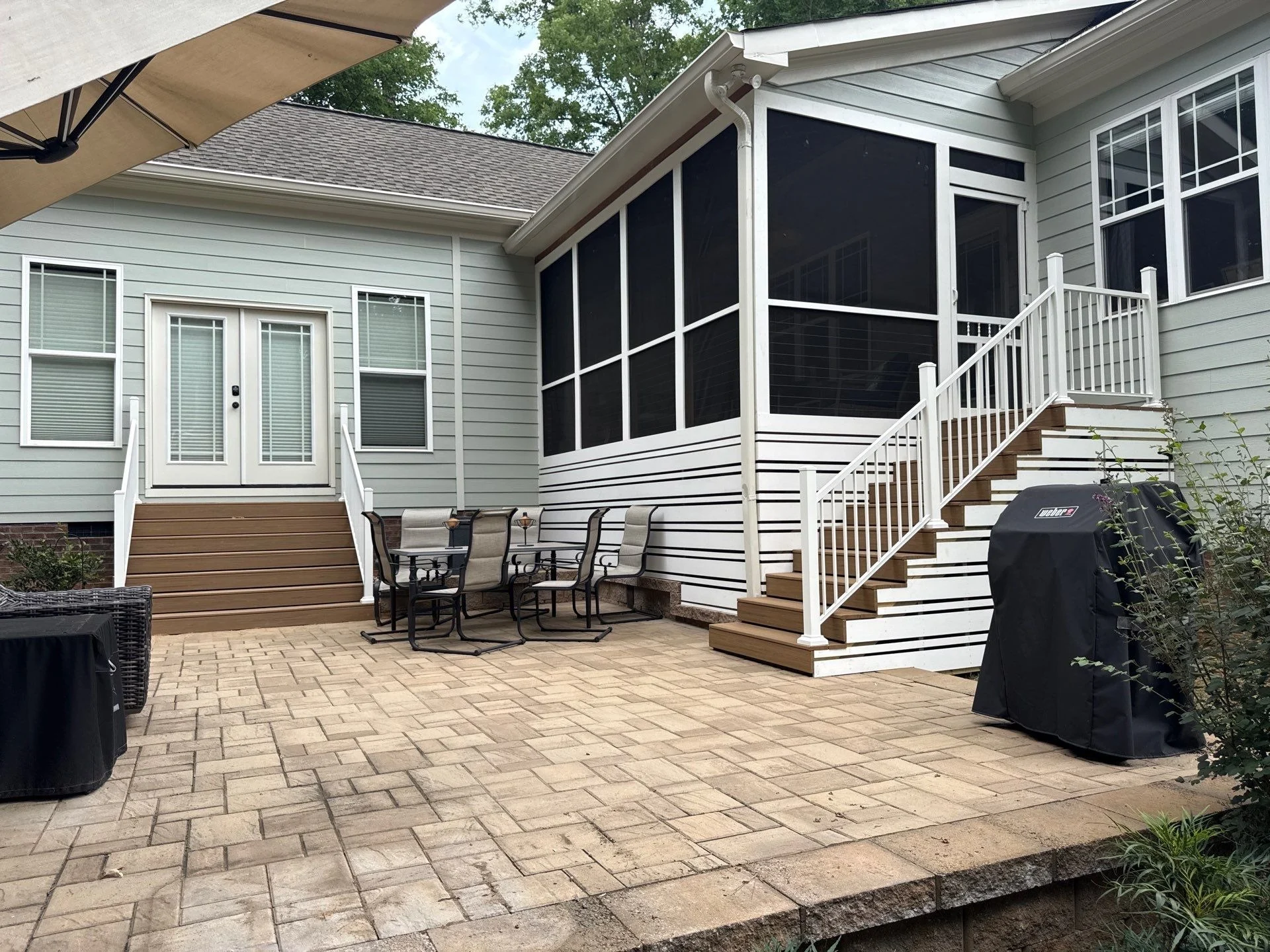 Screened porch with stairs, white railings, composite steps, and a paver patio below.