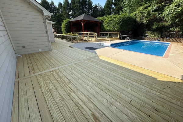 New pressure-treated wood deck connecting a home to an outdoor swimming pool and gazebo.