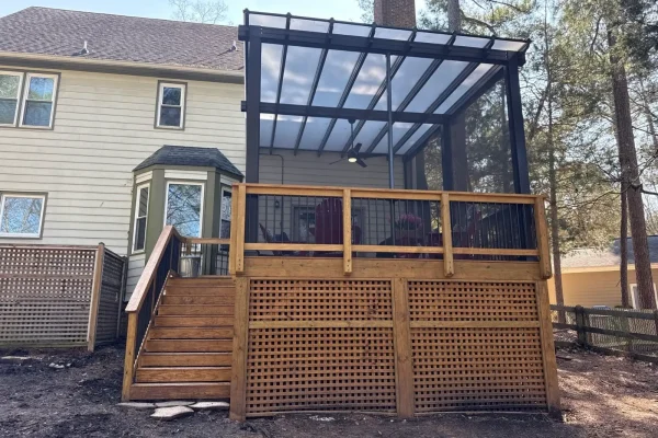 Elevated wood deck with stairs and a covered outdoor living area featuring a black frame and clear roof panels.
