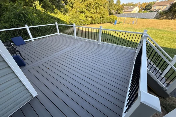 Gray composite deck with white railing posts and black balusters overlooking a large backyard.