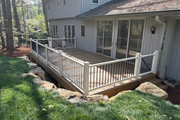 Ground-level composite deck with white posts, black balusters, and landscaped stone edging along the backyard.