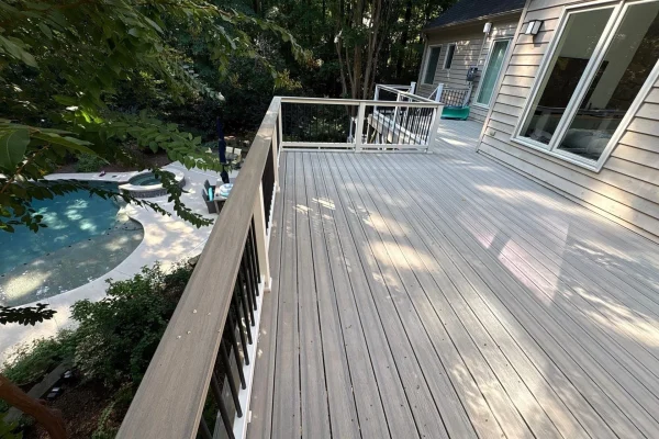 Light composite deck with black balusters overlooking a backyard pool and spa.