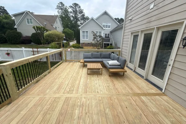 New pressure-treated wood deck with black balusters and outdoor seating beside the home.